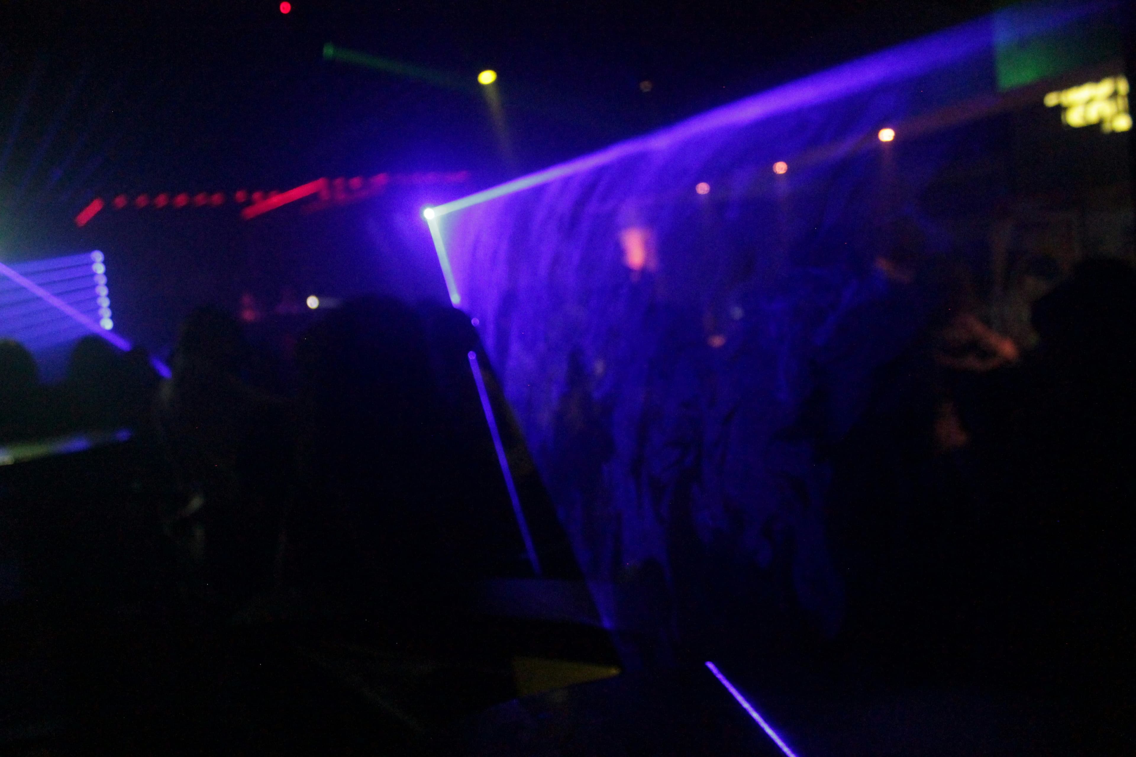 Vibrant laser beams in purple and blue cutting through dark nightclub atmosphere